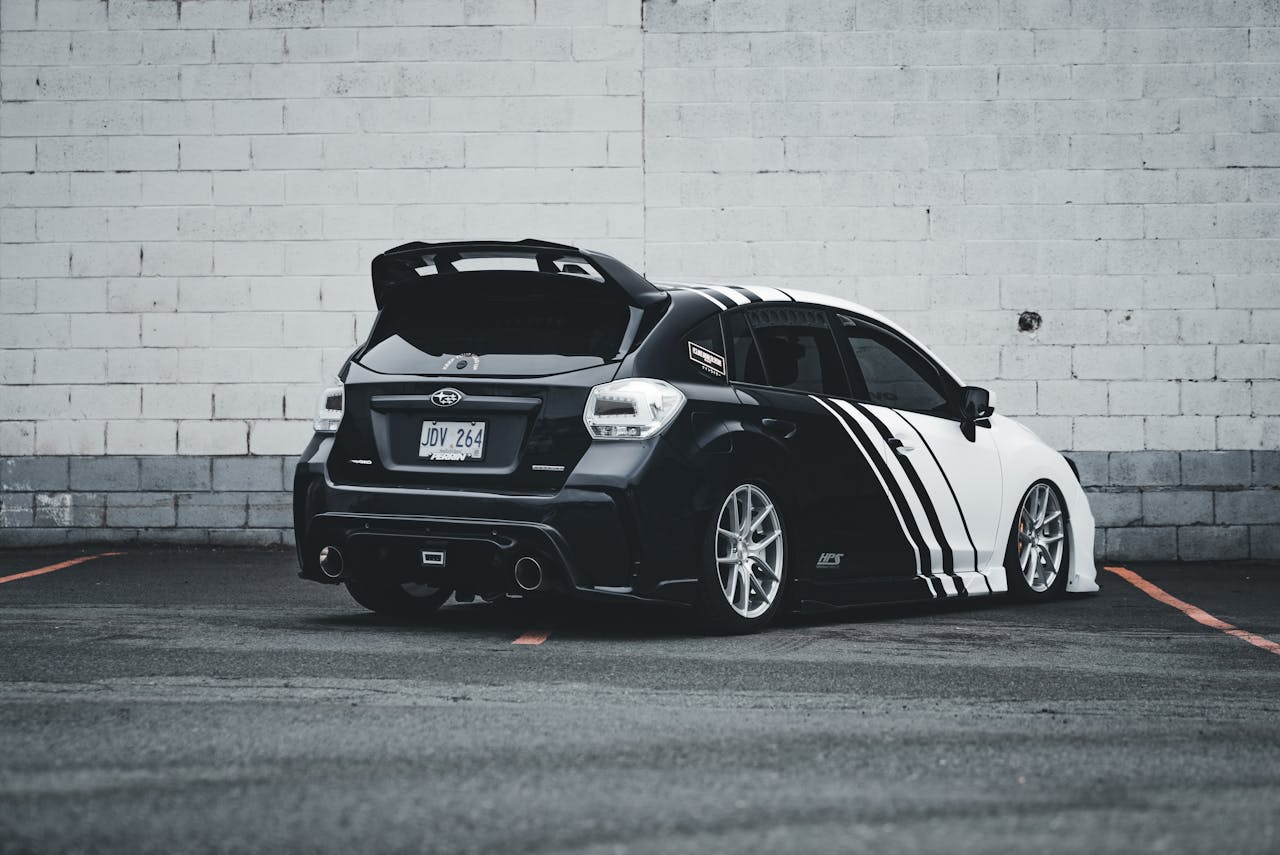 Back view of a customized black and white Subaru WRX sports car parked in an urban setting.